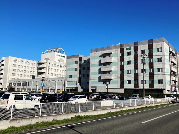 大きな建物の山形済生病院の外観。手前には駐車場と道路が見えます。