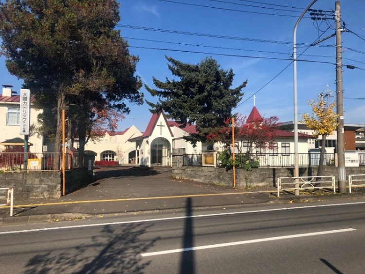 木々に囲まれた大館カトリックこども園の正面玄関。建物の屋根には十字架が見えます。