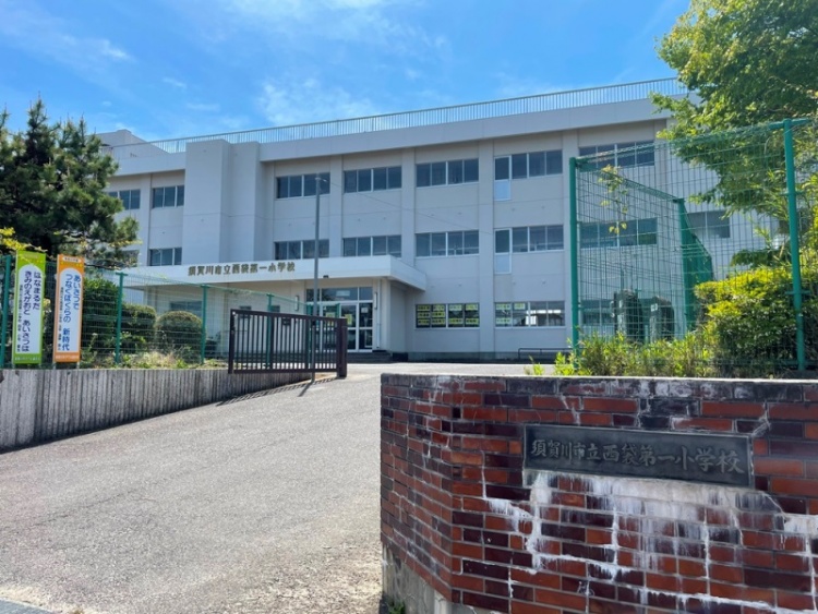 白い3階建ての須賀川市立西袋第一小学校の外観。赤いレンガの門とその先に続く道が見えます。