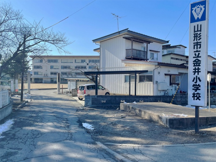 白い外壁の山形市立金井小学校校舎の外観。校舎へ続く道が見えます。