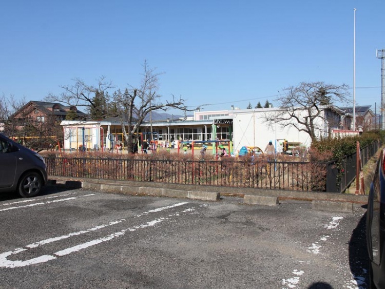 駐車場から見た保原幼稚園の外観。木々が植えられており、子どもが遊んでいます。