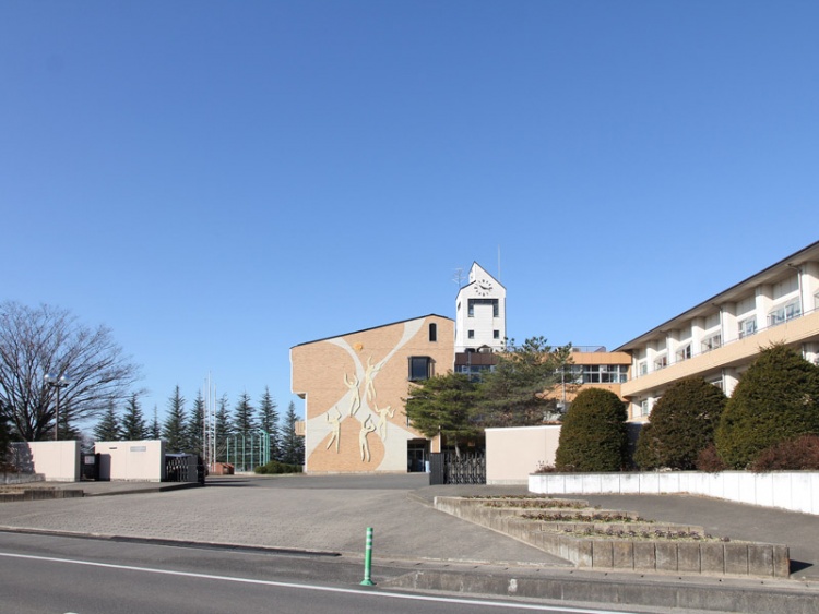 オレンジ色のレンガと時計台が特徴的な桃陵中学校の校舎の外観。広い前庭と植栽が見えます。