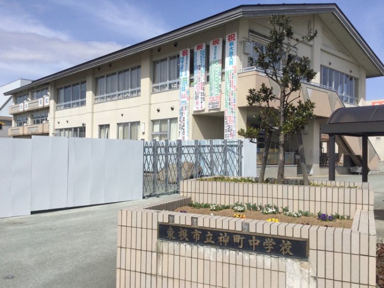 東根市立神町中学校校舎の外観。正面に花壇と植栽があり、垂れ幕が設置されています。
