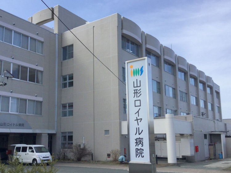 灰色の多層建物の山形ロイヤル病院の外観。駐車場もあります。