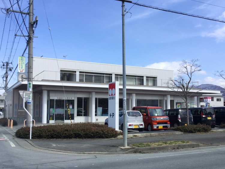 白い建物の山形銀行東根支店の外観。駐車場に数台の車が停められています。