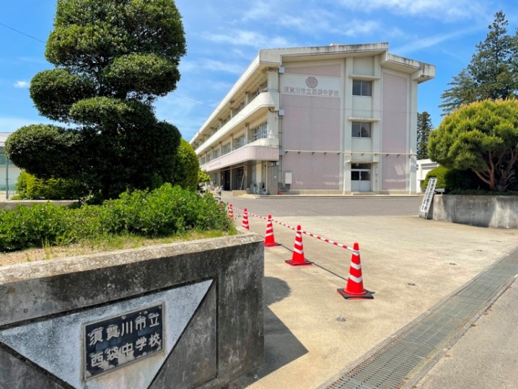 須賀川市立西袋中学校の校舎と外観。赤と白のパイロンが並んでいて木々が植えられています。
