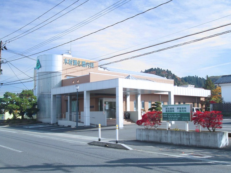 オレンジと緑の文字が特徴的な木村消化器内科医院の外観。駐車場と植栽が見えます。