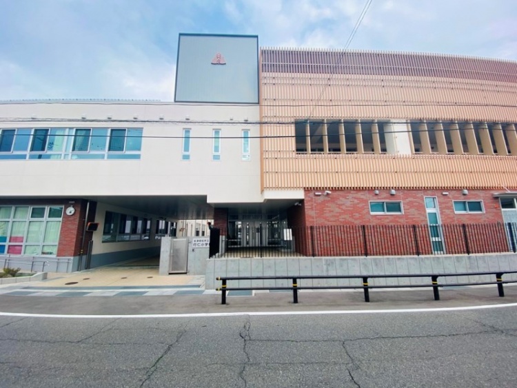赤とオレンジのレンガ調が特徴的な行仁小学校校舎の外観。手前には道路が見えます。