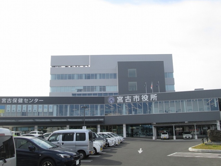 グレーとダークグレーの外壁が特徴的な宮古市役所の外観。手前には駐車場がありたくさんの車が停められています。建物には宮古保健センターの文字が見えます。