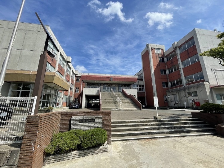 白い壁と赤い壁が特徴的な泉中学校の外観。正面に大きな階段と看板が見えます。