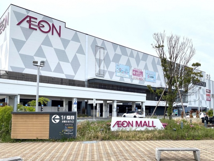 グレーの三角幾何学模様が特徴的なイオンモールいわき小名浜店の外観。手前には木々が生え右奥には駐車場が見えます。