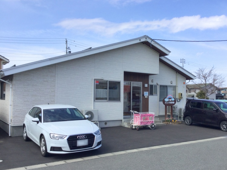 白い外壁の平屋建ての大森にじいろ保育園の外観。駐車場にはたくさんの車が停められています。