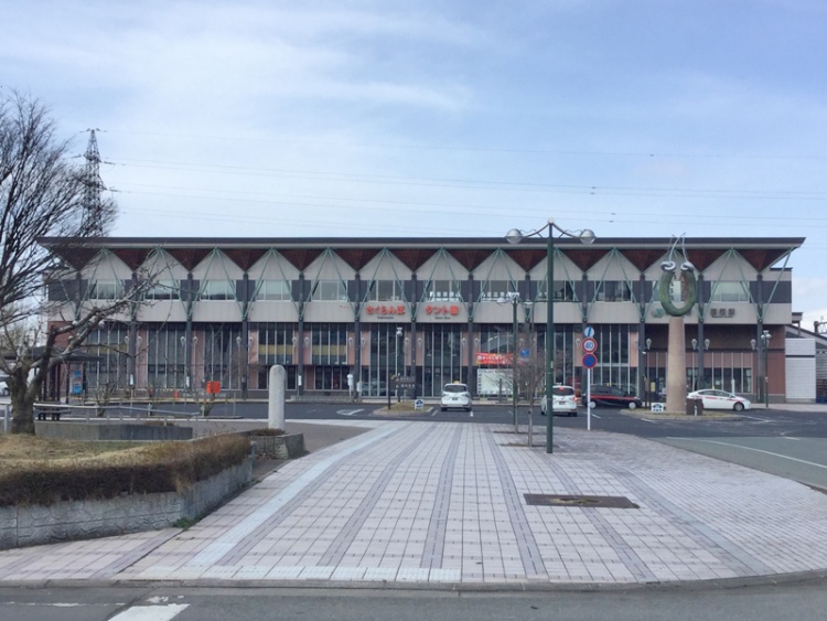 JRさくらんぼ東根駅の正面外観。三角屋根とガラスが特徴的な建物で、駅前には車と駐車スペースが見えます。
