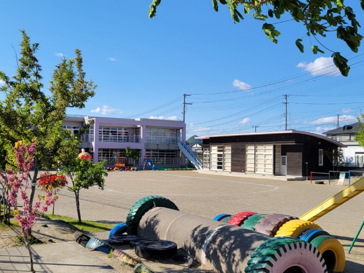 ピンクの外壁が特徴的なもみじヶ丘幼稚園の外観。園庭には鉄棒やタイヤが設置されています。