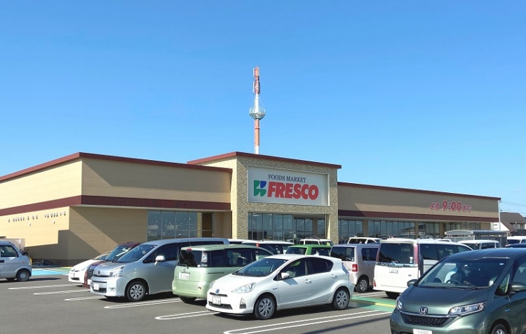薄黄色の外壁が特徴的なFRESCO矢本店の外観。駐車場にはたくさんの車が停められています。