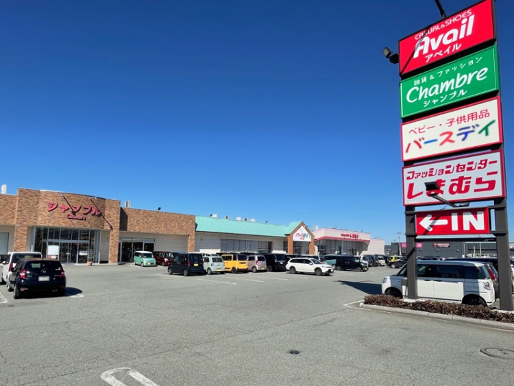 嶋ファッションモールの外観。店舗の看板にはアベイル、シャブル、バースデイ、しまむらが見え、駐車場には数台の車が停められています。