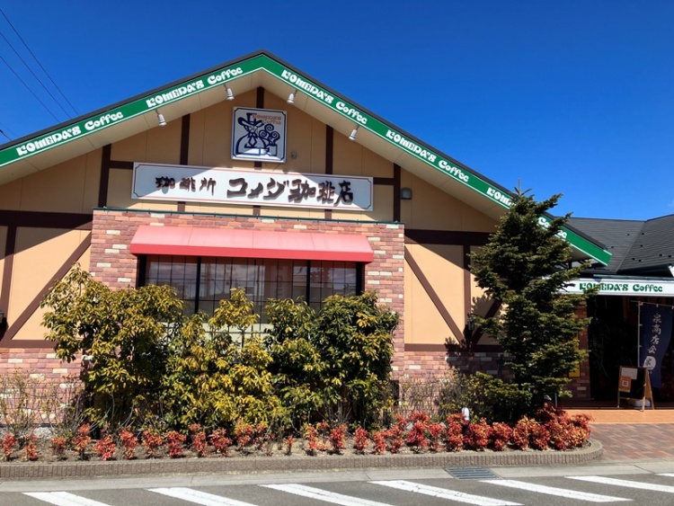 赤と茶色のレンガ調外壁の建物で、コメダ珈琲店いわき泉店の正面外観。建物の前には低木が植えられている。