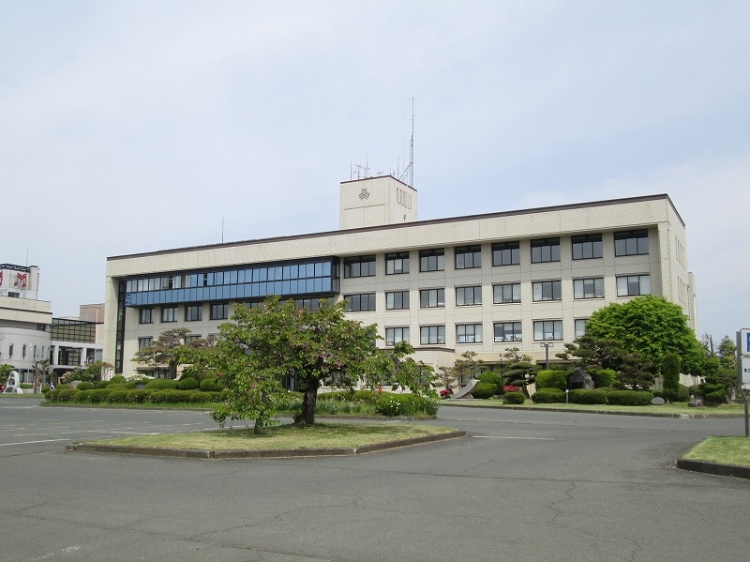 広い駐車場と庭がある白い4階建ての矢巾町役場の建物。