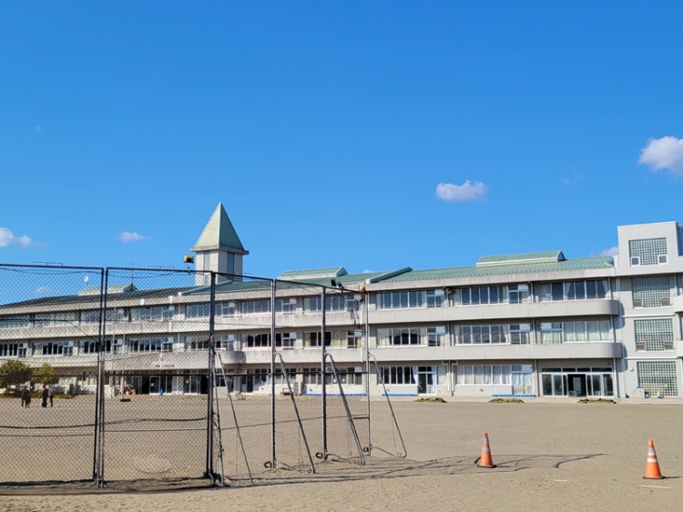 白の外壁と緑の屋根が特徴的な3階建ての小野小学校校舎の外観。屋根の上には尖塔が見えます。