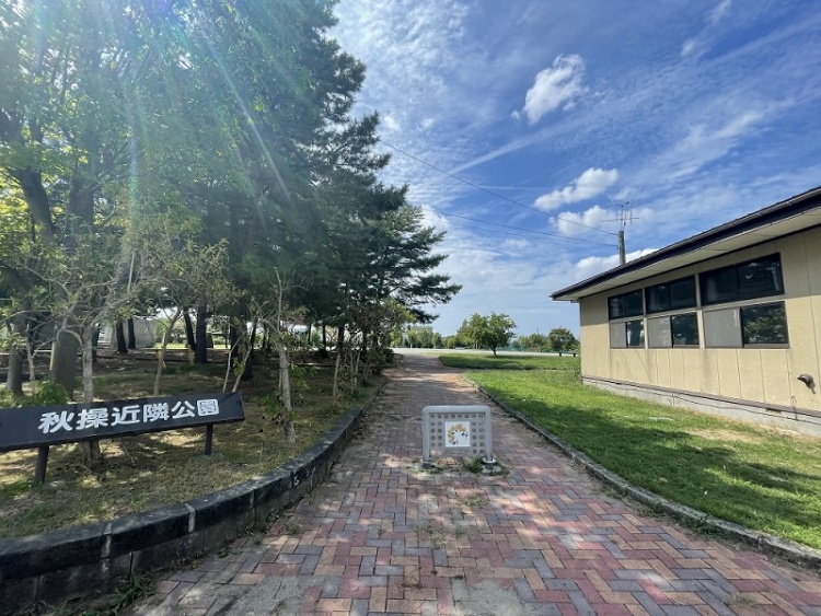 秋操近隣公園の入り口。左側に樹木、右側に建物があり、レンガの道が続いています。