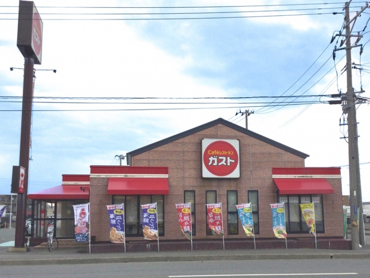 レンガ風の建物に赤い看板と日除けが特徴的なガスト酒田北店の外観。前に色とりどりの旗が並んでいます。