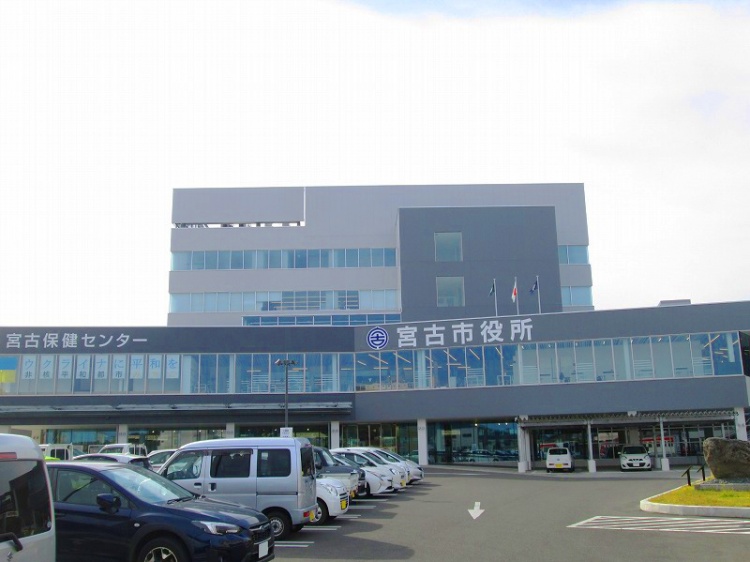 グレーとダークグレーの外壁が特徴的な宮古市役所の外観。手前には駐車場がありたくさんの車が停められています。建物には宮古保健センターの文字が見えます。