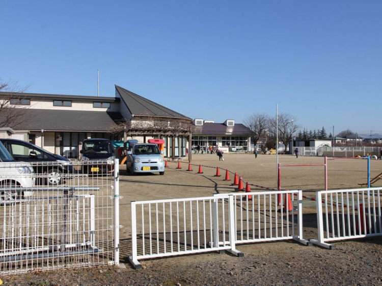茶色い三角の屋根が特徴的な保原保育園の外観。広場があり車やコーンが並んでいます。