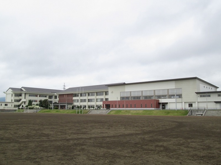 校庭から見た矢巾中学校の校舎。広いグラウンドと複数の建物が見える。