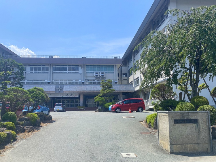 山形市立第四中学校の校舎外観。駐車場には数台の車があり、周囲には木々が植えられています。
