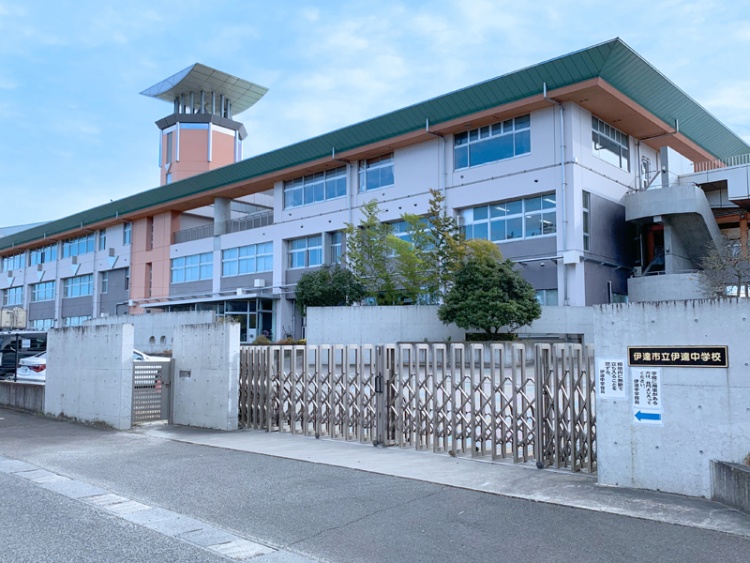 伊達市立伊達中学校の校舎の外観。鉄製のフェンスと植栽が見えます。