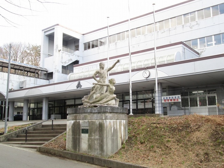 白い外壁が特徴的な城南中学校の外観。二体の人物像が配置された石造りのモニュメントが立つ学校です。