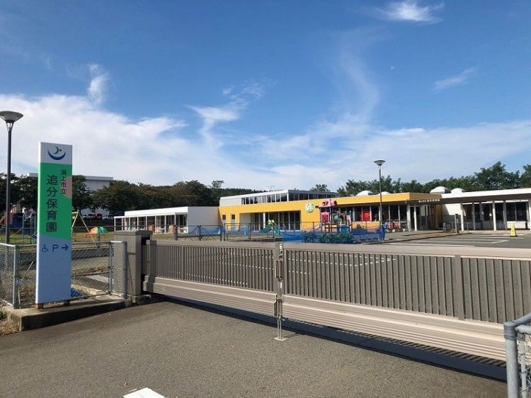追分保育園の建物と入口のゲート。左側に看板が立っており、敷地内には遊具が見えます。