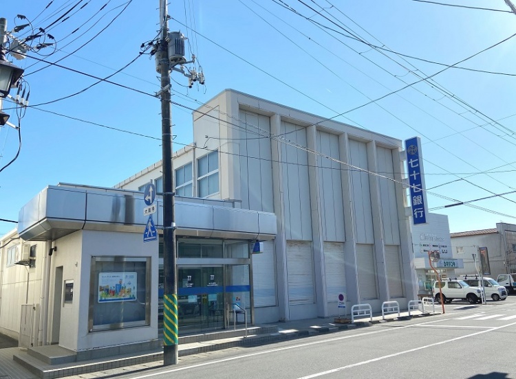 青い看板が特徴的な七十七銀行矢本支店の外観。入口に銀行のロゴが見えます。