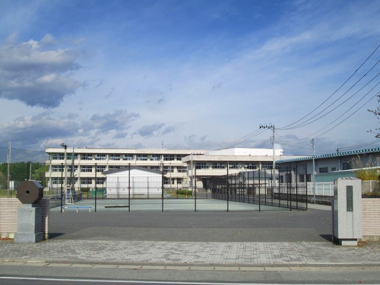 広場とフェンスの奥に見える桜町中学校校舎の外観。手前には道路が見えます。