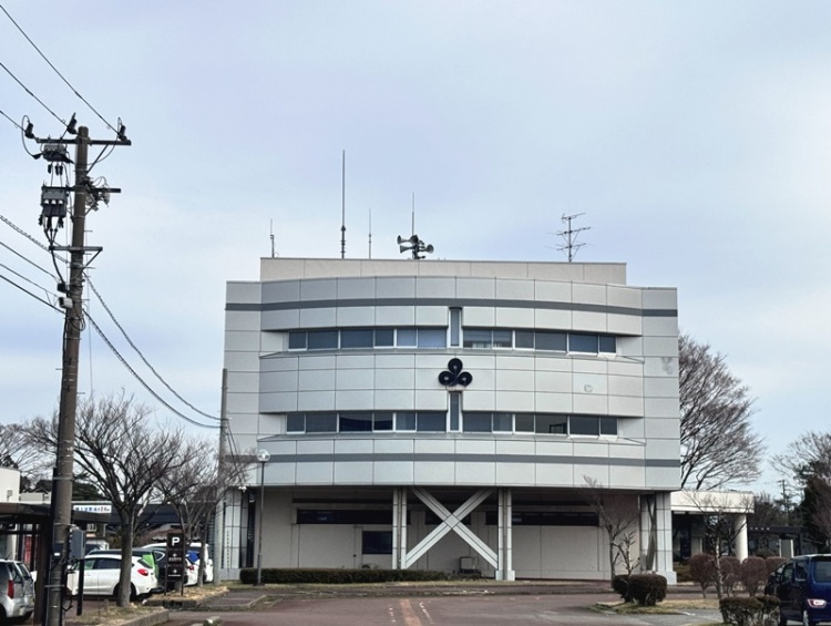 三川町役場です。屋上には複数のアンテナが立っていて、電柱や駐車場も見えます。