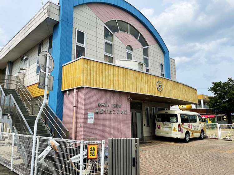 青と黄色が特徴的な希望ヶ丘こども園の外観。白い送迎バスが停まっています。