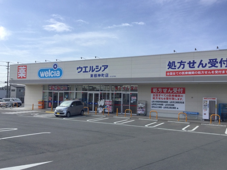 ウエルシア東根神町店の外観。駐車場には数台の車が停められています。薬局の看板や処方せん受付の表示が見えます。