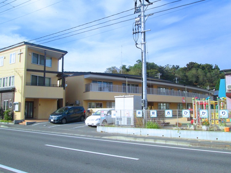 黄色の外壁が特徴的な宮古ひかりこども園の外観。駐車場に車が2台駐車しており、道路沿いに位置しています。