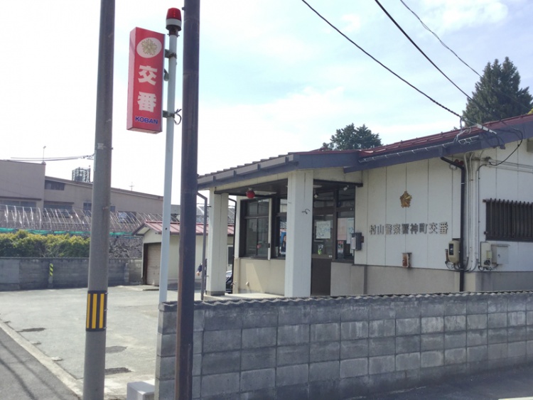 白い建物の村山警察署神町交番の外観。駐車場、植栽が見えます。