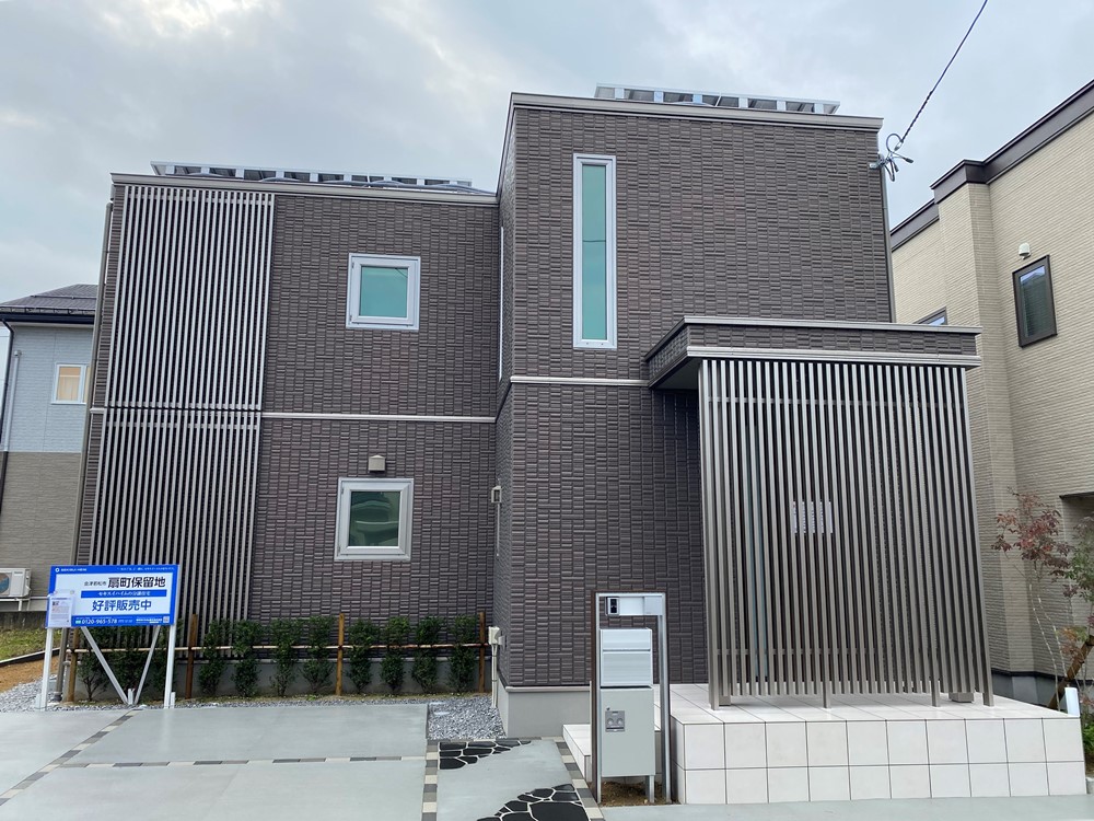 ブラウンの外壁の２階建て住宅外観の住宅。縦格子の目隠しが設置された玄関です。好評販売中と書かれた看板が建てられています。