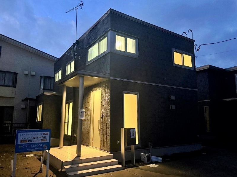 ダークグレーを基調とした二階建て住宅の外観です。玄関には小さな階段があり、縦長の窓がスタイリッシュに配置されています。