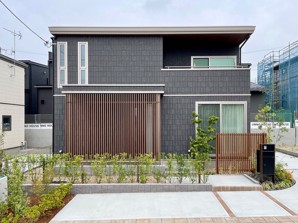 ダークグレーの外壁と木目調ルーバーを基調とした２階建て住宅のB棟外観。前庭には植栽が植えられています。