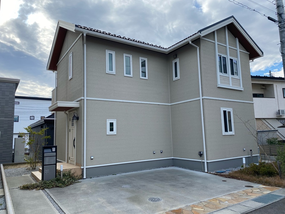 落ち着いたベージュの外壁に三角屋根が映える、駐車場付きの2階建て住宅です。