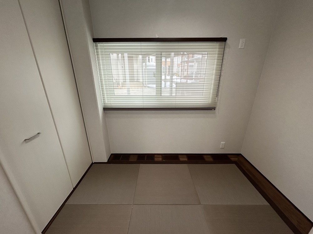 シンプルで落ち着いた和室の一角。畳敷きの床が心地よい雰囲気を演出し、窓にはブラインドがかかっている。左側には白いクローゼットがあり、収納にも便利な空間。