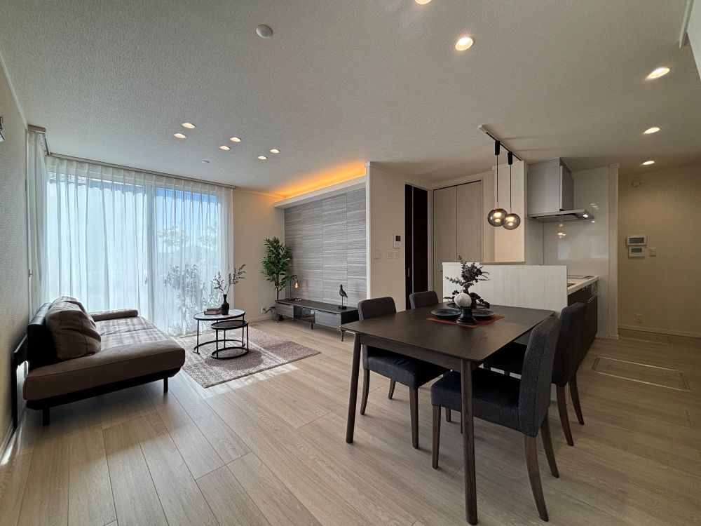 白とグレーを基調としたリビングダイニングキッチン。ダイニングテーブル、ソファ、丸テーブルが配置されています。右奥にキッチンが見えます。