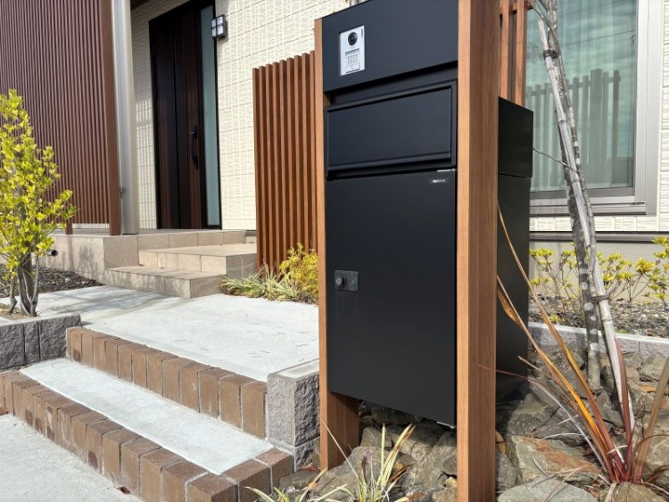 Ａ棟の玄関。黒い宅配ボックスが設置され、階段と植栽が植えられています。