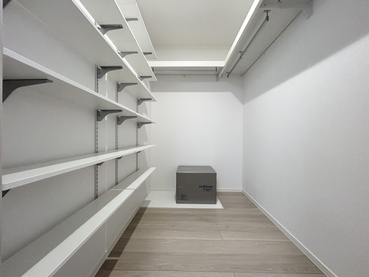 壁一面に棚が並び、上部にはハンガーパイプも備えられた収納スペースで、衣類や日用品を効率よく整理できるよう工夫されています。