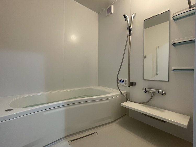 清潔感のあるユニットバスです。浴槽、シャワー、カウンター、鏡、収納棚を備え、追い焚き操作パネルも設置されています。