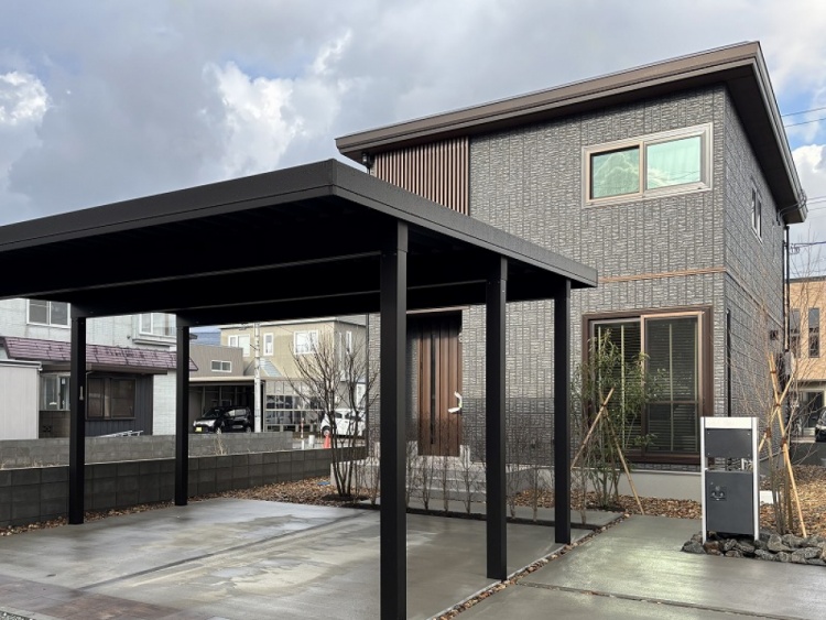 シックな黒の外壁に木目のアクセントが映えるモダンな2階建て住宅。カーポートやアプローチもスタイリッシュに整えられ、洗練された佇まいを感じさせます。