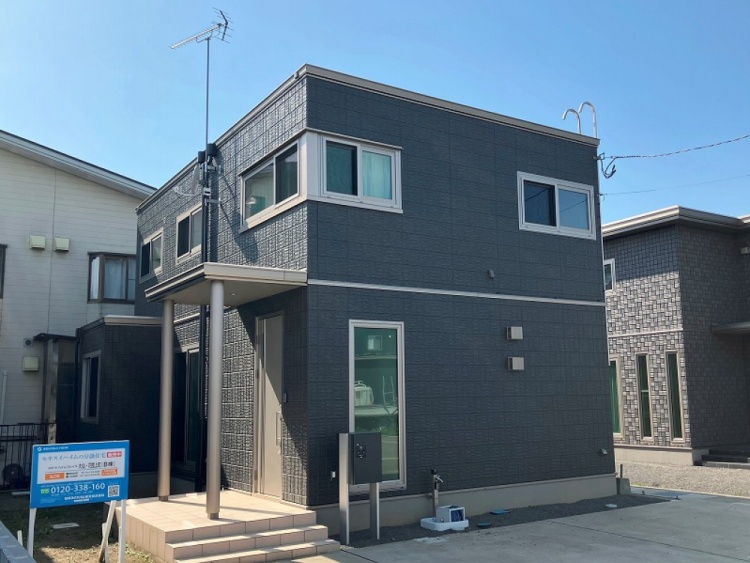 ダークグレーを基調とした二階建て住宅の外観です。玄関には小さな階段があり、縦長の窓がスタイリッシュに配置されています。